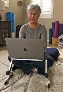 Joyce sitting cross-legged on cushion on floor while working on computer 