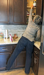 Joyce standing and stretching to reach into top cupboard