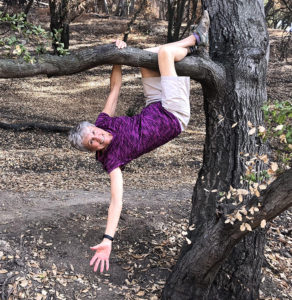 Joan at 80 hanging with one arm from a tree