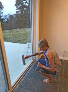 Joan washing patio window in a squat